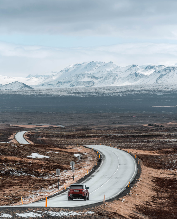 Car driving on winding road with mountains in the background and clouds in the sky