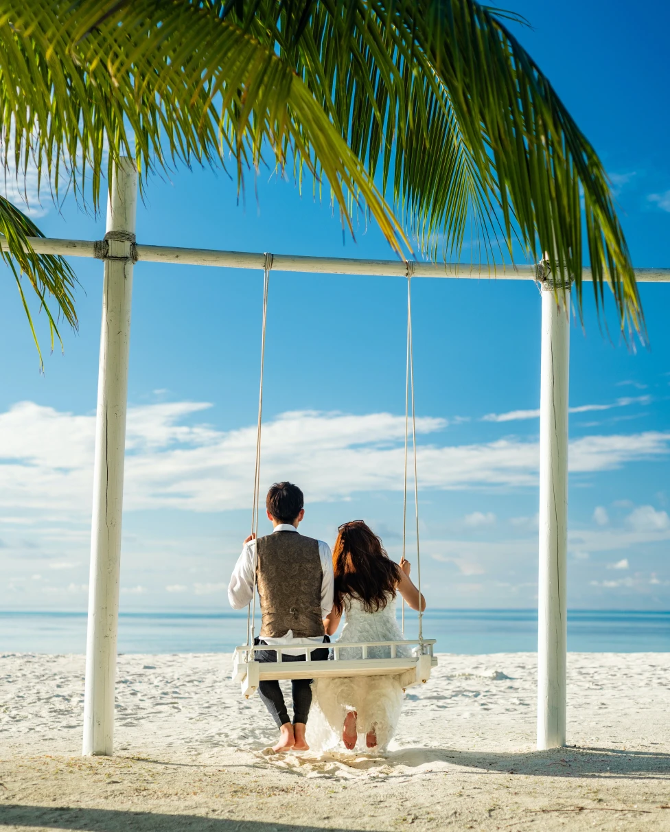 A couple sitting on a swing on a tropical beach. 