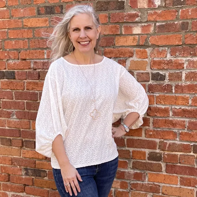 Picture of Karen in a white top standing in front of a brick wall 