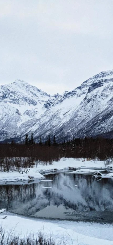 Snowy mountains behind icy lake during a chilly winter day in Anchorage, Alaska. 