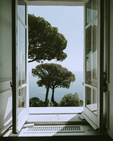 open white window overlooking green trees and the sea below