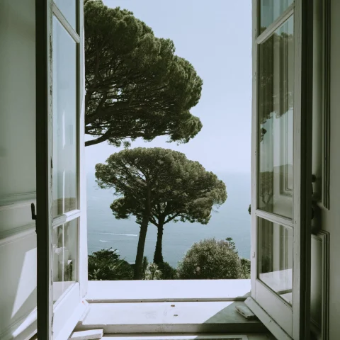 open white window overlooking green trees and the sea below