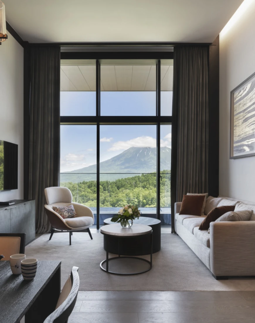 sleek hotel room with floor-to-ceiling windows overlooking a green mountain