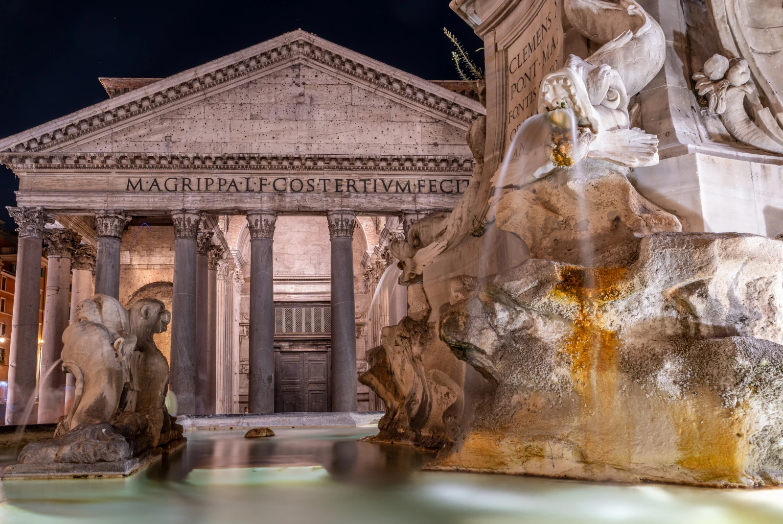 The Pantheon in Rome, Italy at night lit up with white lights reflecting on the stone.