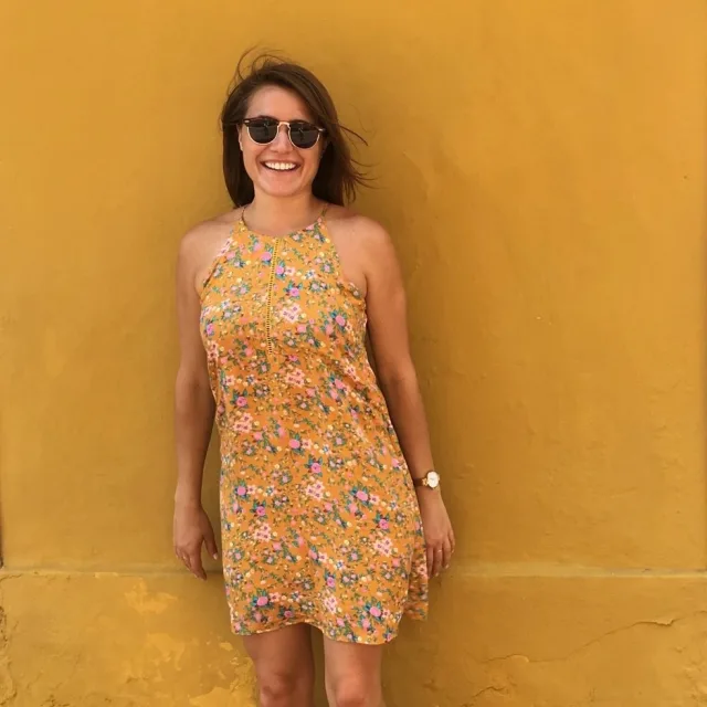 Travel advisor avery laberge wears a yellow dress and stands in front of a yellow wall