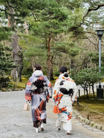 Two individuals in traditional kimonos strolling through a lush Japanese garden.