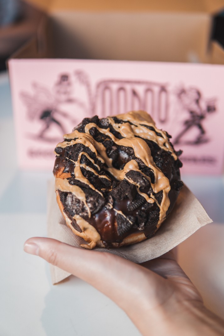 A black and tan oreo doughnut with a pink VooDoo Doughnuts box in the back from Portland travel.