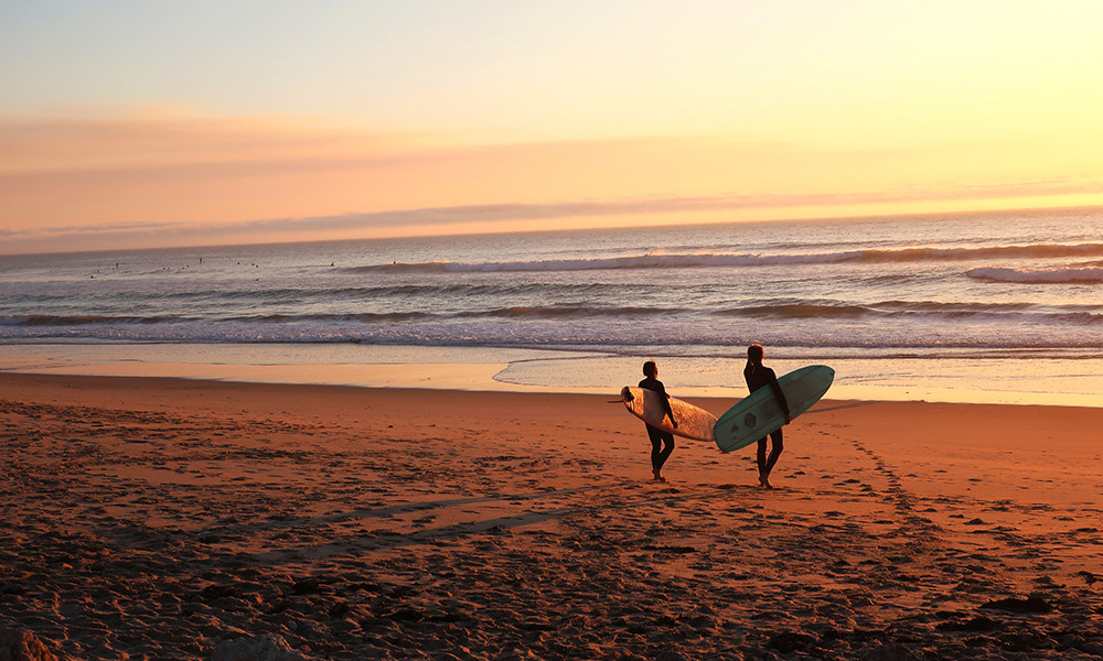two people holding surfboards walking on the sun into the waves in the ocean at sunset
