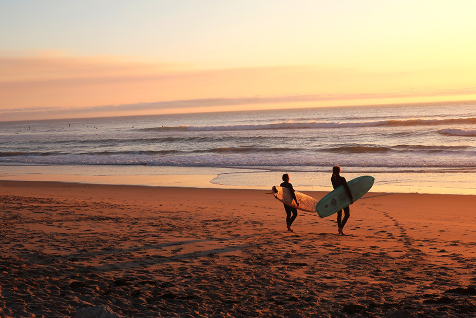 two people holding surfboards walking on the sun into the waves in the ocean at sunset