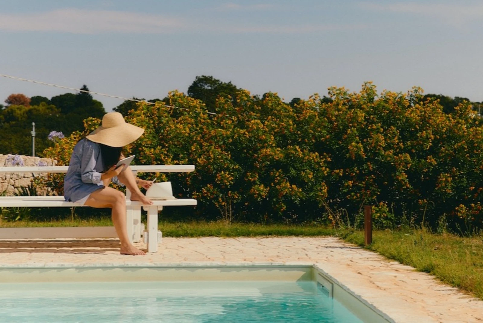woman in a sun hat sitting on the edge of an outdoor pool