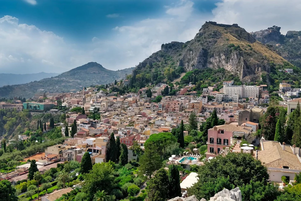 a coastal town nestled into the hillside with colorful stone buildings and green trees