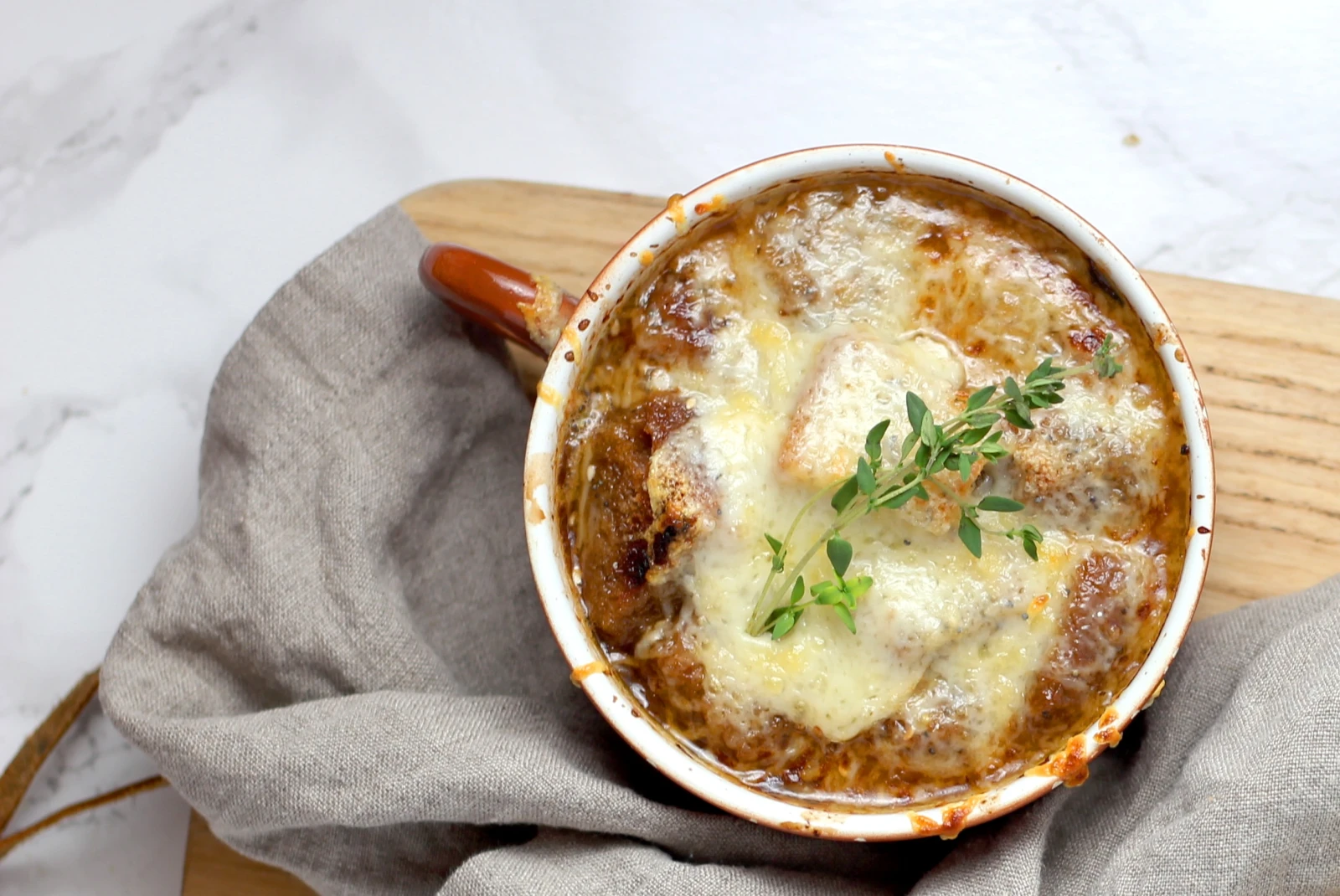 Hot onion soup in a mug topped with fresh herbs on a wooden cutting board