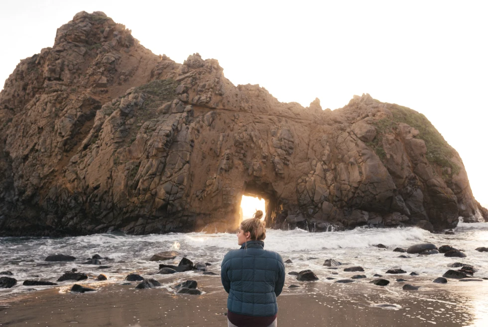 A woman standing in front of a rock formation in Big Sur, California. 