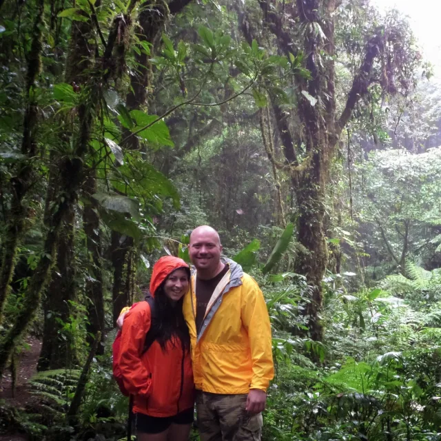 Travel Advisor Kim Weldon with her partner in both red and yellow raincoats standing in front of the jungle.