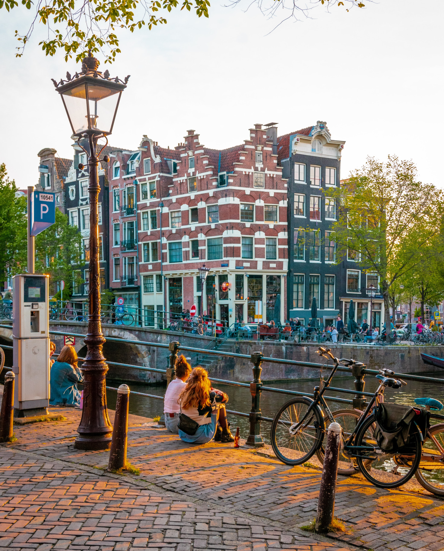 People sitting next to bikes and canal with buildings in the background during daytime