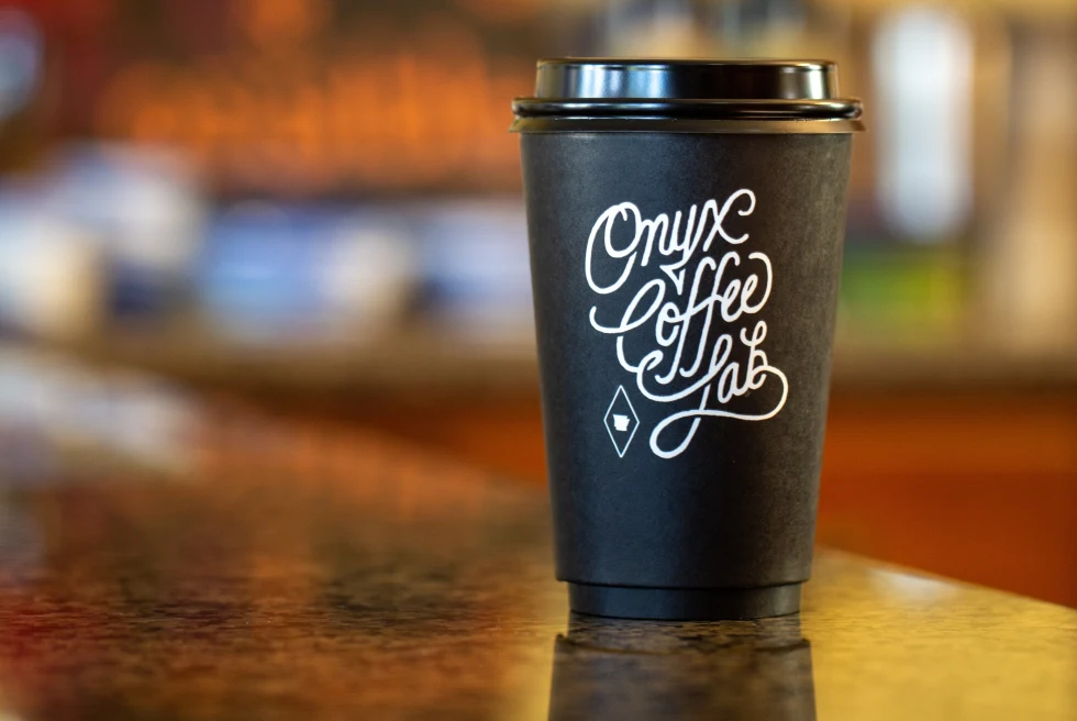 A black paper coffee cup with "Onyx Coffee Lab" written on it in white cursive font.