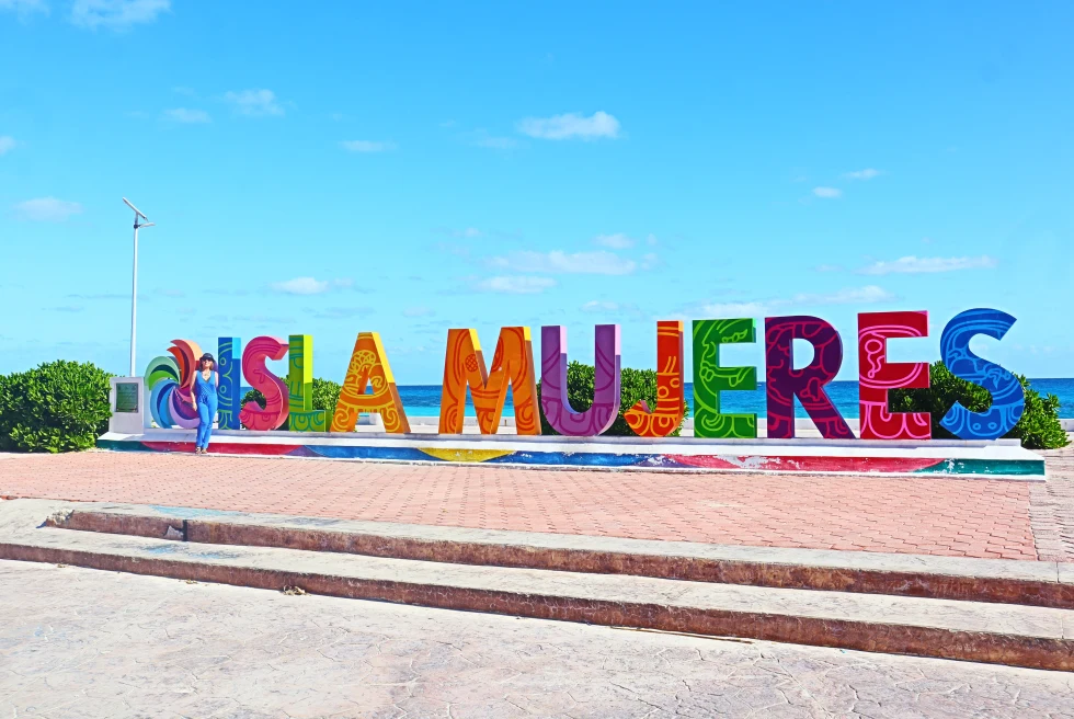 Colorful letters spelling "Isla Mujeres" with sunny sky with ocean in the background