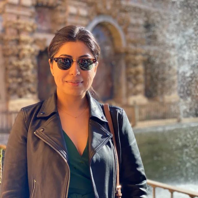 Travel Advisor Urvashi Marwah with sunglasses on, a brown leather jacket in front of a stone building.