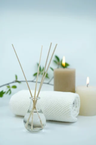 Candles, a white towel and a branch of greenery staged on a table.
