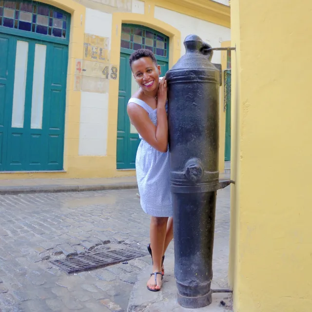 A picture of Kenya wearing a dress on a stone street surrounded by teal and yellow buildings