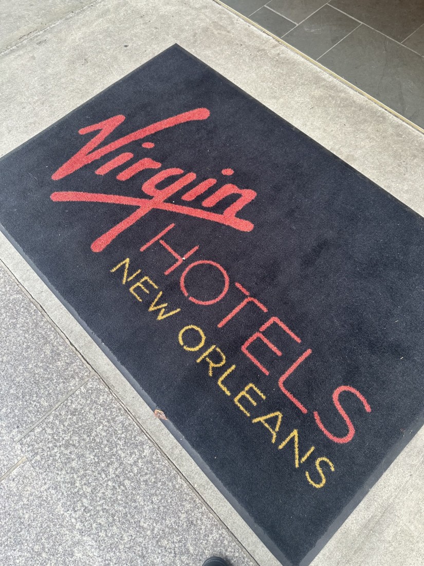 A black welcome mat with the text, Virgin Hotels New Orleans in red and yellow