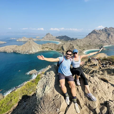 A couple posing for a photo at the top of a mountain by the water