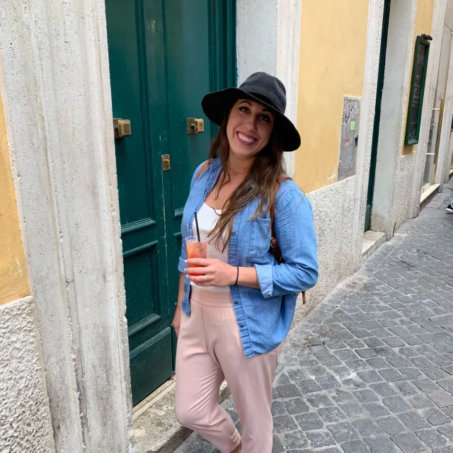 Travel Advisor Justina Cerra Lucas with a jean jacket, pink jumpsuit, in front of a green door.
