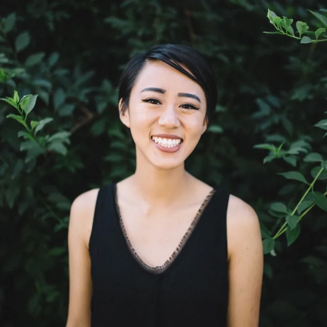 travel advisor Allyson Calenda with short black hair and a black tank top smiling in front of green leaves