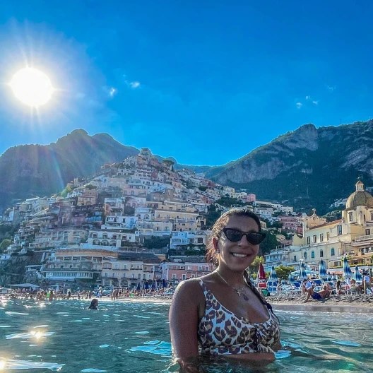Travel advisor Samar Asfour posing in water with Italy in the background.