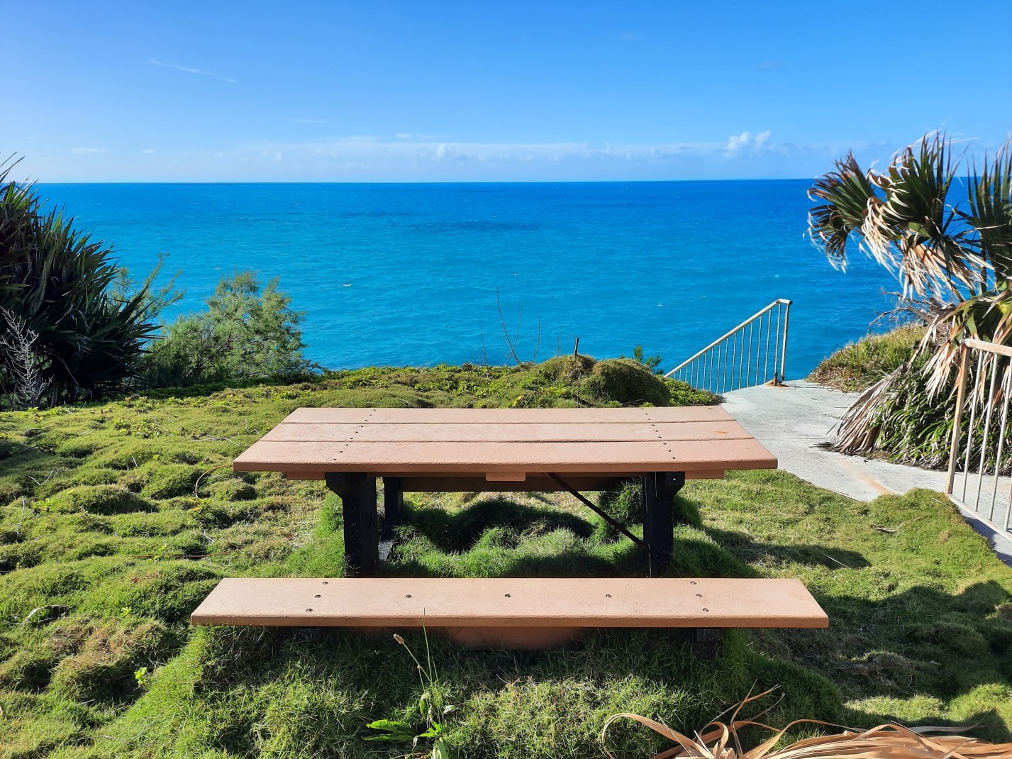 Wood picnic table on grass with ocean and blue sky