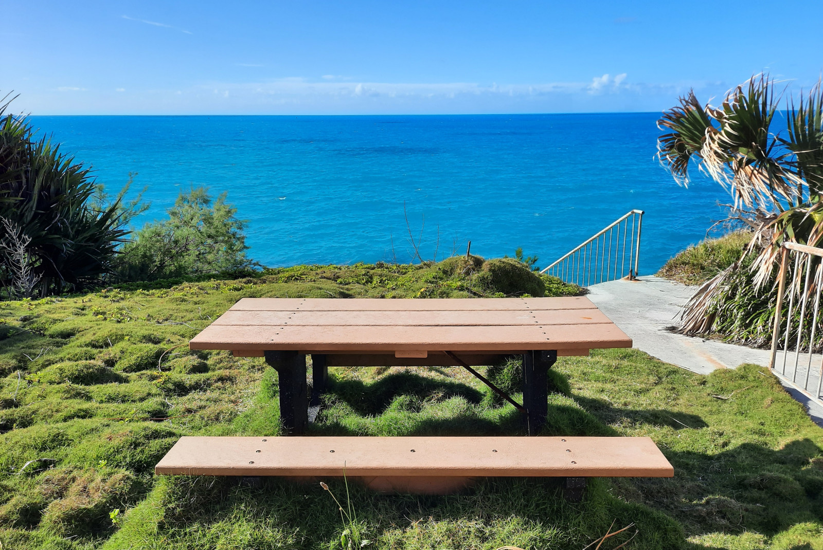 Wood picnic table on grass with ocean and blue sky