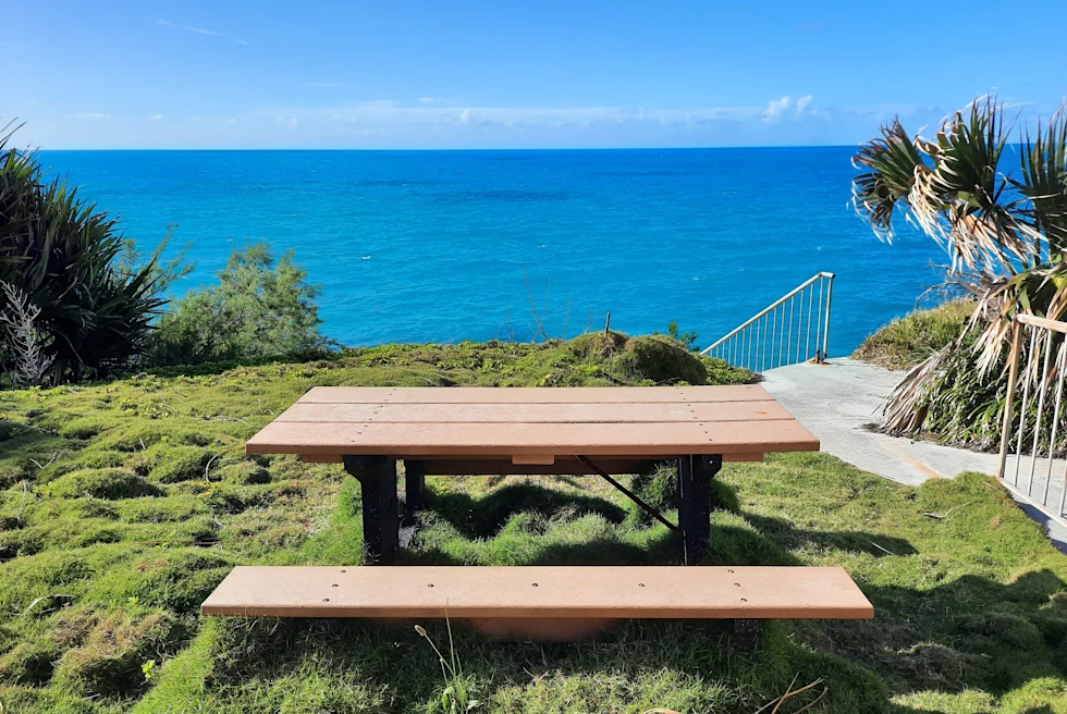 Wood picnic table on grass with ocean and blue sky