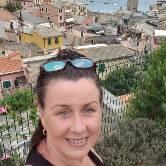 Travel Advisor Natasha Jiovino standing on a hilltop with colorful houses and the sea in the distance.