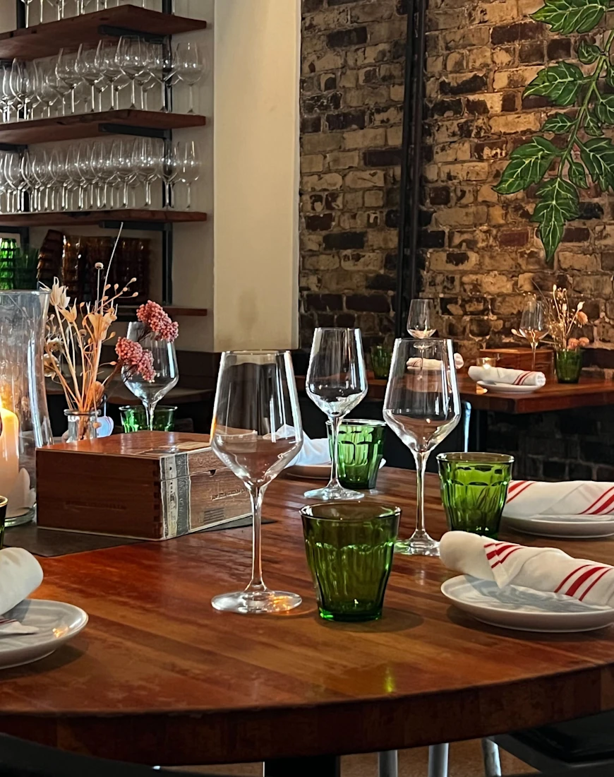 a round set table with green water glasses and wine glasses in front of a brick wall