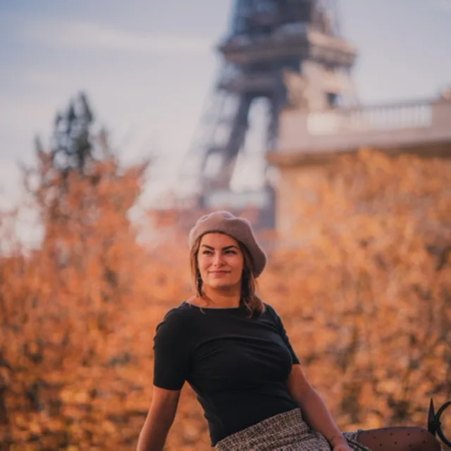 travel advisor Jovana Pellerito sits in front of the Eiffel Tower and autumn trees wearing a black shirt and baret