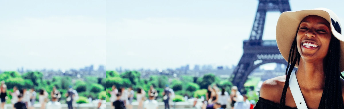 Woman wearing black dress and brimmed hat stands in front of the Eiffel tower in Paris with people in the distance