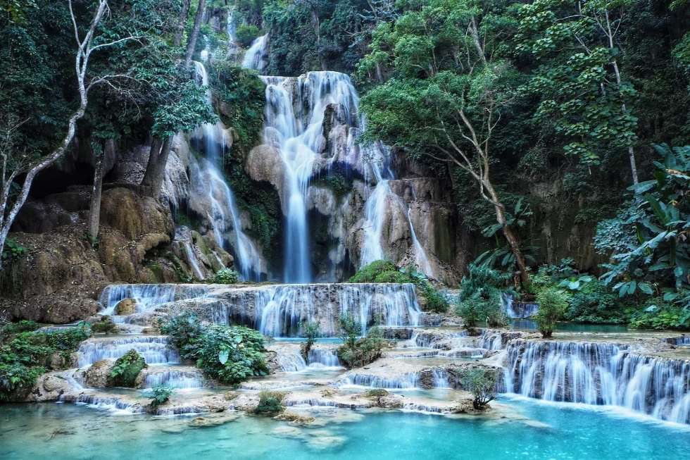 Waterfall surrounded by green tress and merging into a blue lake. 