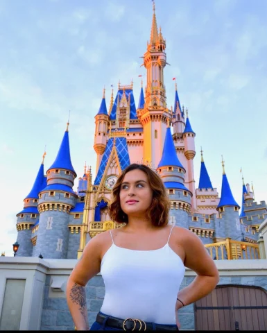 A person posing for a photo in front of the Disney World Castle during the daytime