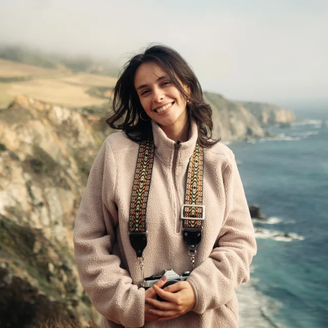 Travel Advisor Michelle Gutierrez in a tan sweater in front of cliffside mountains and the sea.