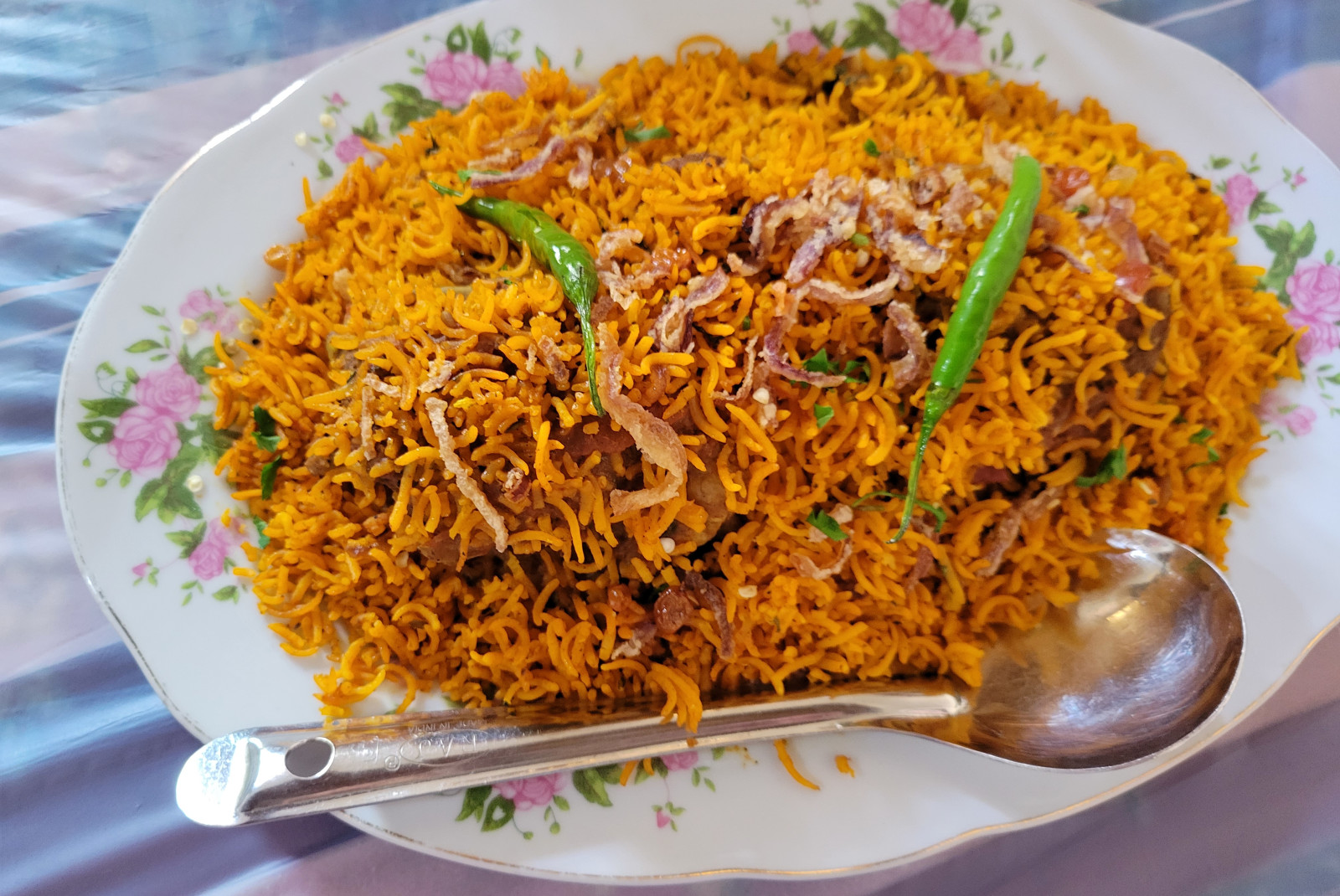 A yellow, saffron rice and green bean dish in the UAE served on a white plate with green and pink floral patterns and a silver spoon.
