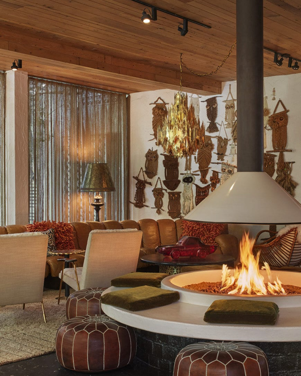 a round fire pit surrounded by leather stools in a room with eclectic artwork