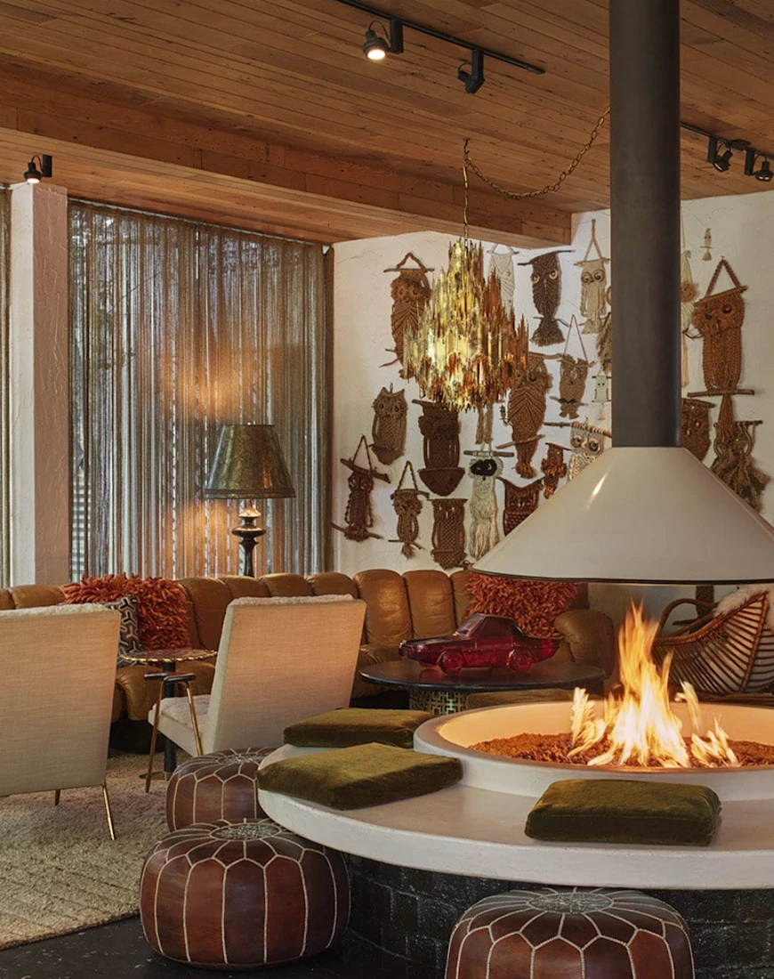 a round fire pit surrounded by leather stools in a room with eclectic artwork