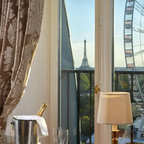 A view out the window of a room in the Regina Hotel Paris of the Eiffel Tower and Roue De Paris, with a table set with champagne and macarons in the foreground.