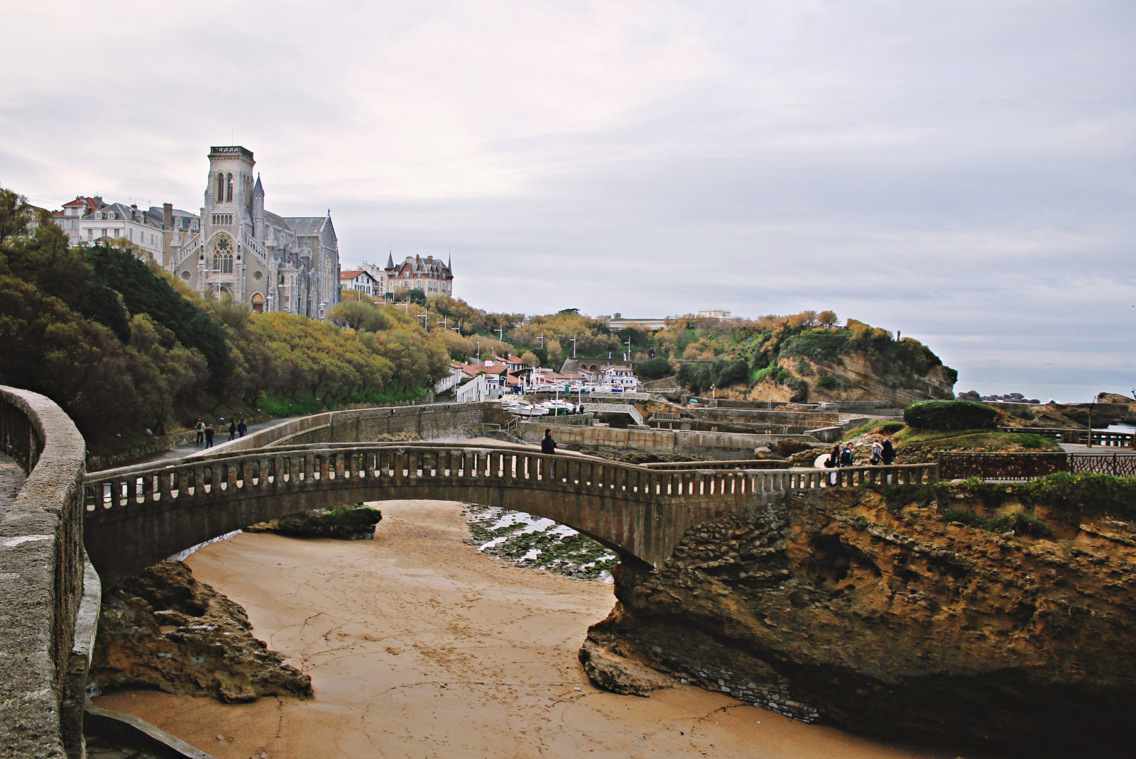 Bridge over sand along coast with building on cloudy day in Biarritz, France