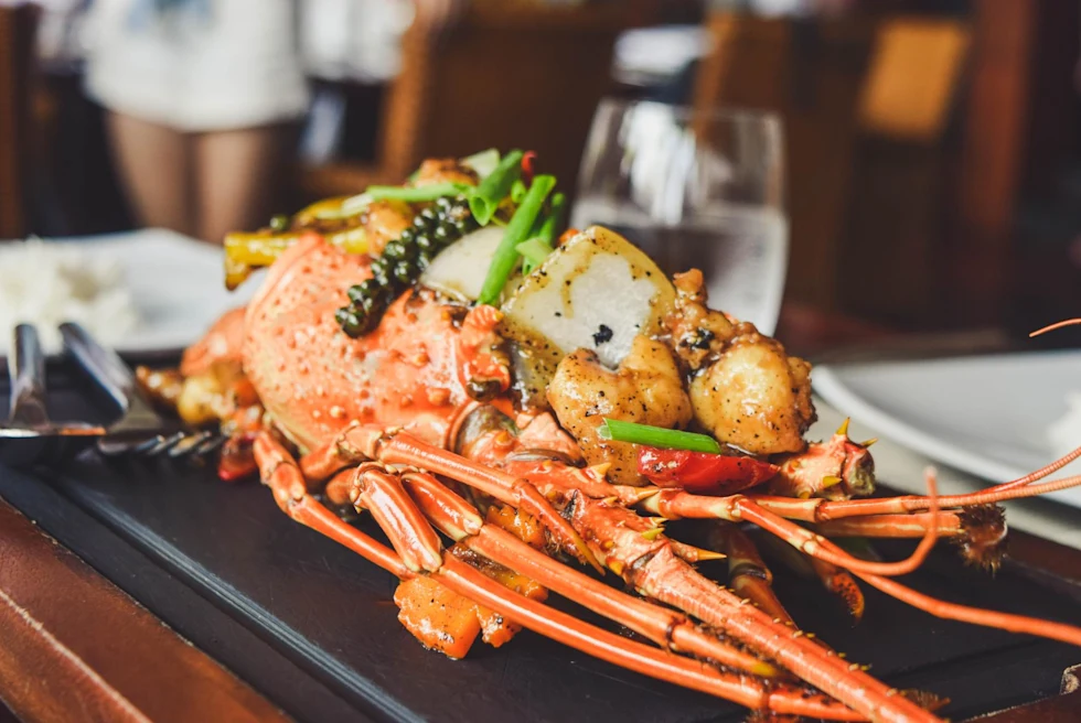 Glazed lobster decorated with vegetables and caviar on table of fine-dining restaurant.