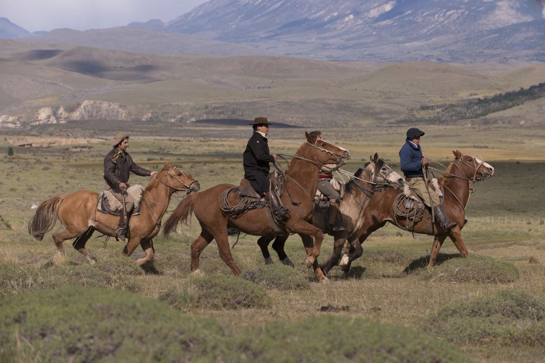 four horses and riders in a valley with mountains in the background