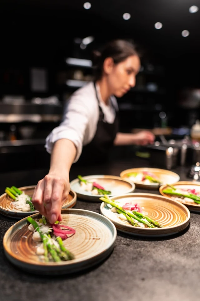 Female chef in white shirt and black apron arranging various plates of food in a fine dining restaurant