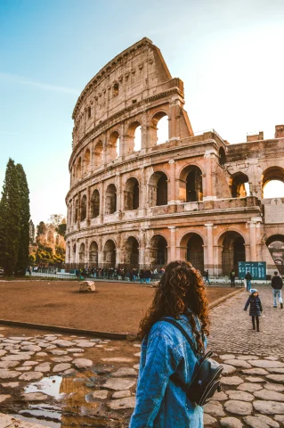 A girl with curly hair standing in front of the Collosseum. 