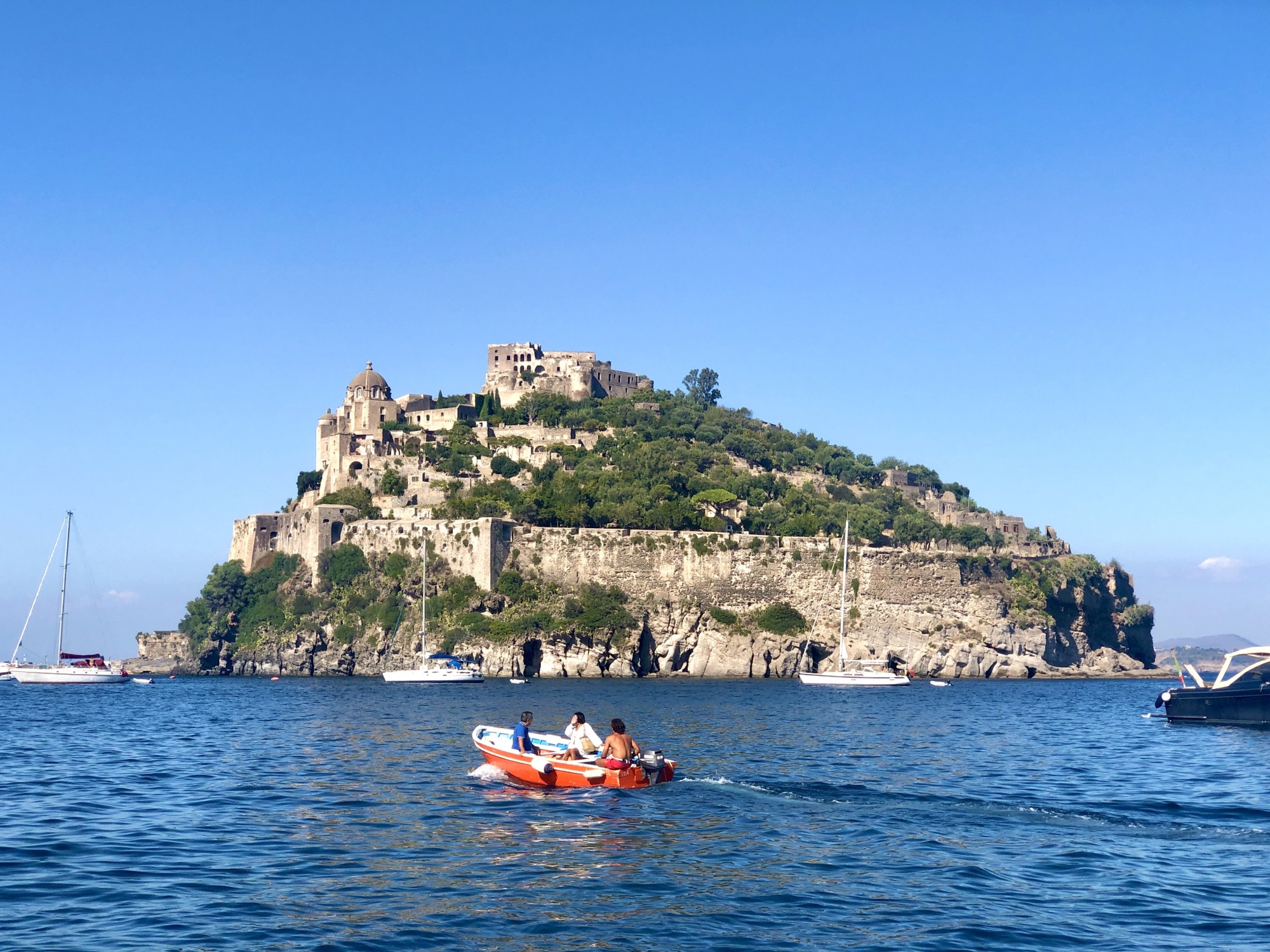 a small red boat approaches rocky island with stone walls