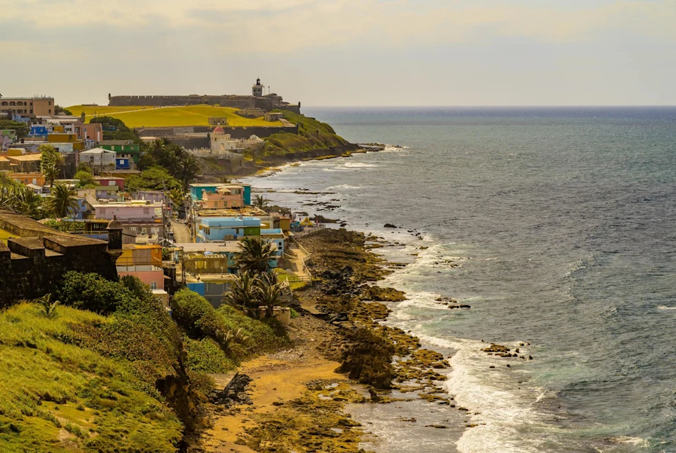view of a coastal city during the day with green hills and colorful buildings